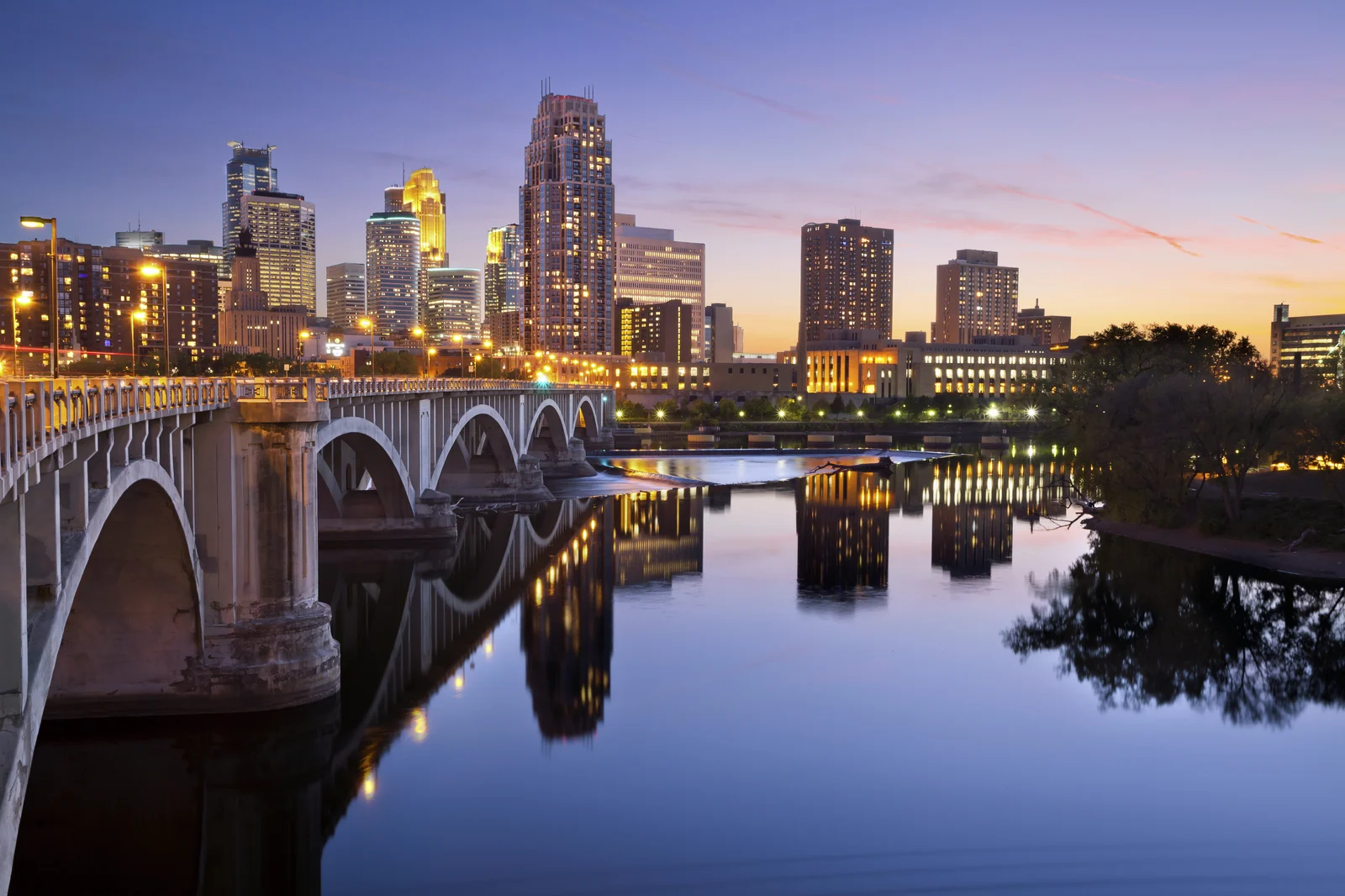 Looking at a city from the far side of a still river where a bridge is crossing